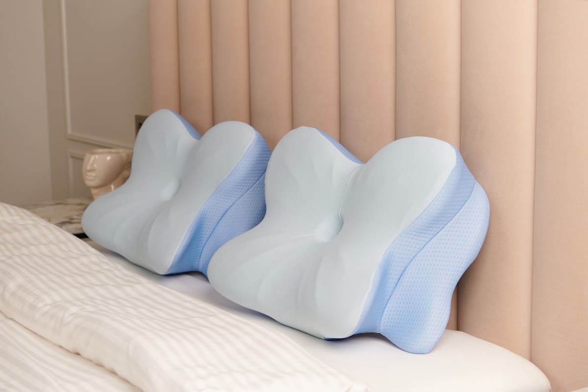Two contoured memory foam pillows resting against an upholstered headboard in a bedroom, seen from the side